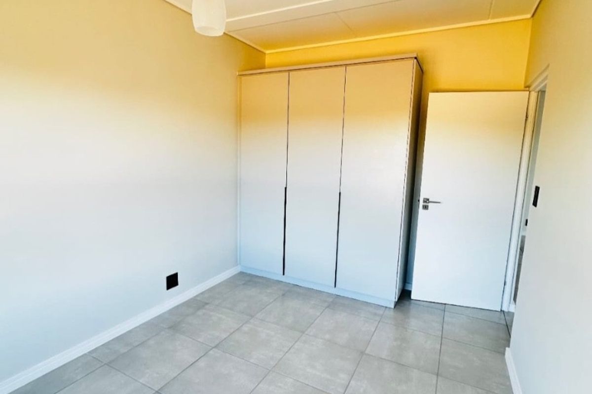 A clean, empty bedroom featuring neutral tiled flooring, a built-in wardrobe, and a modern pendant light fixture.