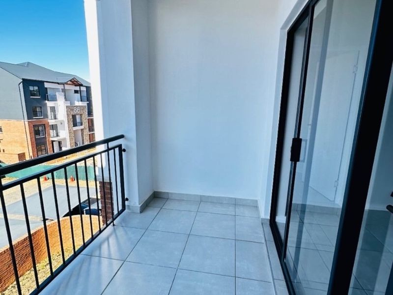 A clean, modern balcony featuring light-colored floor tiles, a black metal balustrade, and a large sliding glass door providing access to the interior.