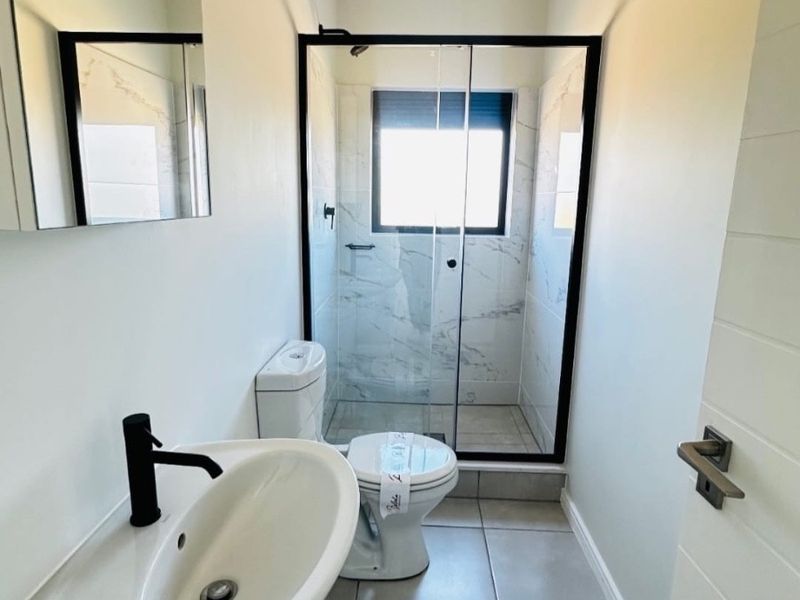 Modern bathroom featuring a wall-mounted basin with black fixtures, a toilet, and a glass-enclosed shower with marble-look wall tiling.