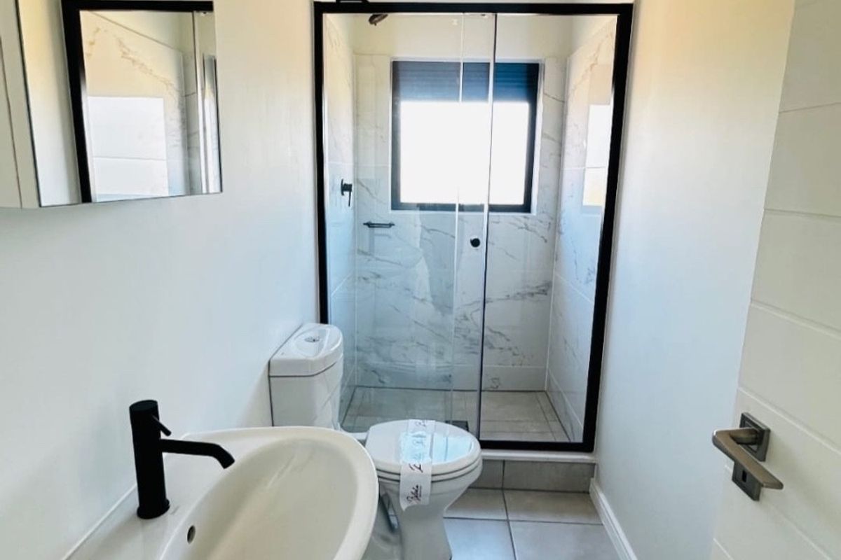 Modern bathroom featuring a wall-mounted basin with black fixtures, a toilet, and a glass-enclosed shower with marble-look wall tiling.