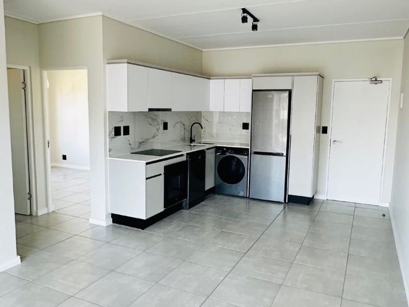 Modern open-plan kitchen featuring sleek white cabinetry, marble-look splashback, integrated appliances, and neutral tiled flooring in a bright, vacant living space.
