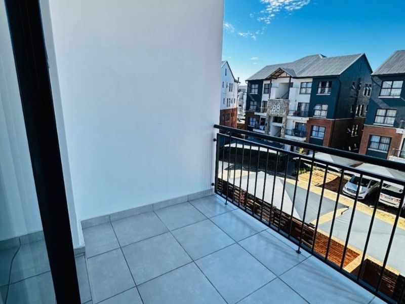 A clean, modern balcony featuring tiled flooring and a secure metal balustrade, offering an open view of the surrounding apartment complex.