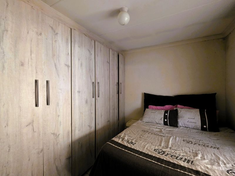 A compact bedroom featuring floor-to-ceiling built-in cupboards with a wood-grain finish, requiring some cosmetic attention to walls and ceiling.