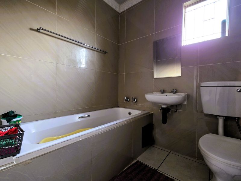 A functional bathroom featuring a built-in bathtub, wall-mounted basin, and toilet, finished with neutral ceramic wall and floor tiles.