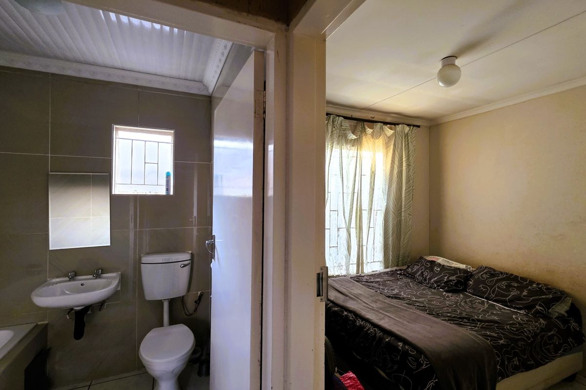 A view showing a bedroom adjacent to a small tiled bathroom with a wall-mounted basin and toilet.