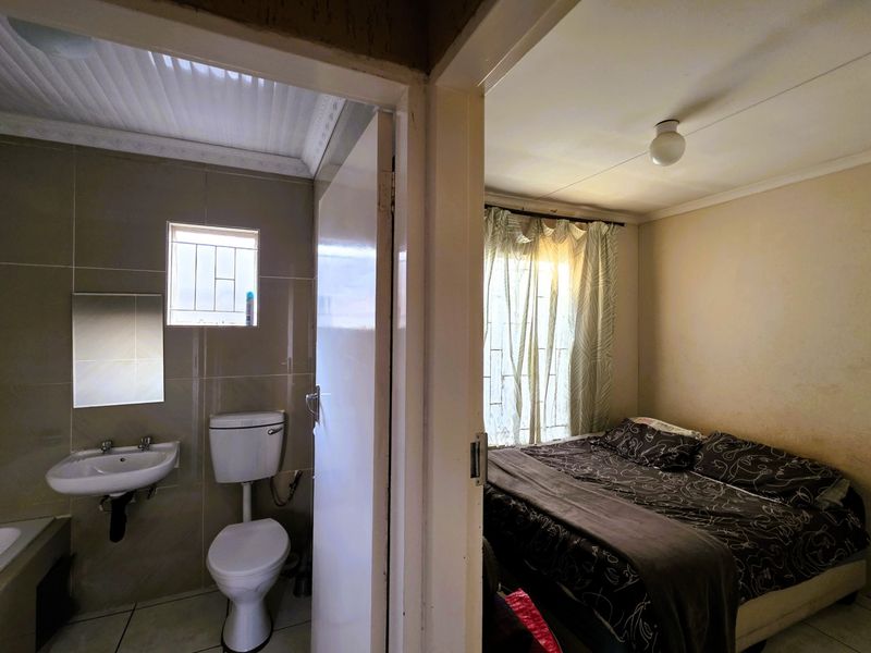 A view showing a bedroom adjacent to a small tiled bathroom with a wall-mounted basin and toilet.