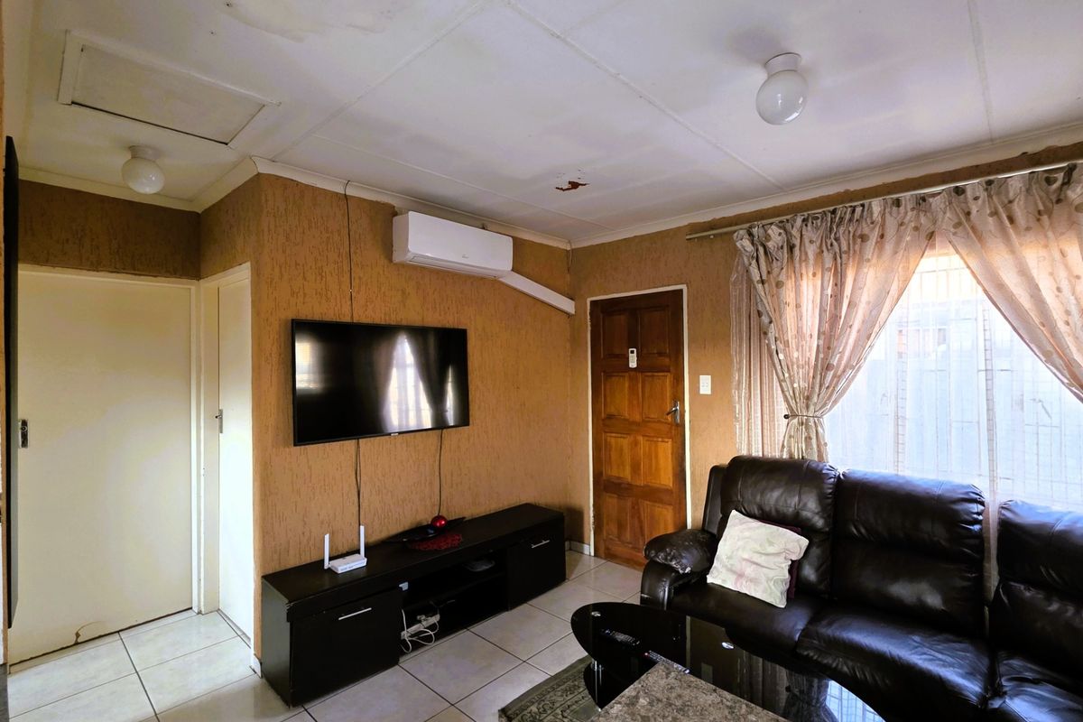 Living room featuring tiled flooring, a wall-mounted air conditioner, and textured wall finishes, with visible signs of ceiling water damage.