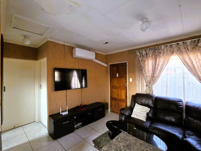 Living room featuring tiled flooring, a wall-mounted air conditioner, and textured wall finishes, with visible signs of ceiling water damage.