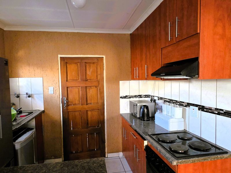 A functional kitchen featuring wood-finish cabinetry, dark laminate countertops, an electric hob with extractor fan, and tiled backsplash.