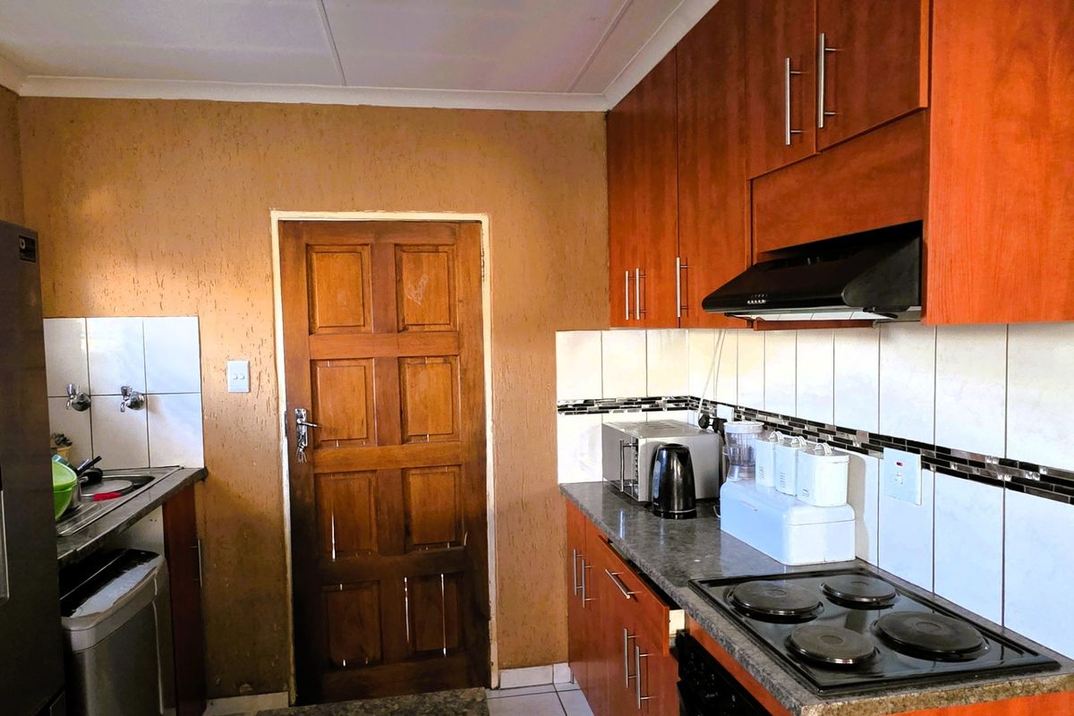 A functional kitchen featuring wood-finish cabinetry, dark laminate countertops, an electric hob with extractor fan, and tiled backsplash.