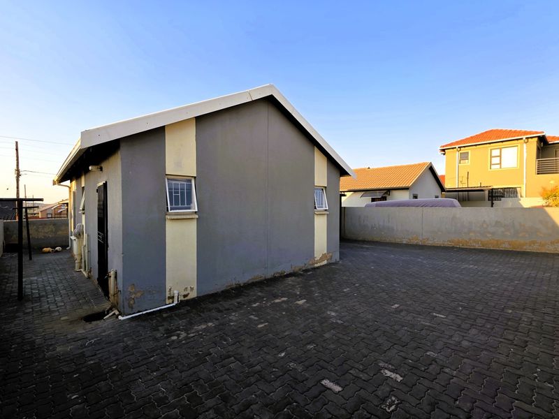 Rear exterior view of the property featuring a paved courtyard area and perimeter walling with visible wear to the exterior wall finish.