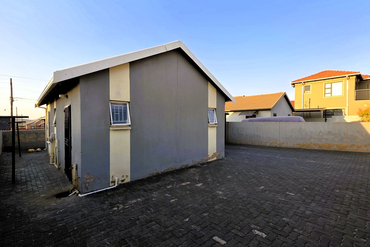 Rear exterior view of the property featuring a paved courtyard area and perimeter walling with visible wear to the exterior wall finish.