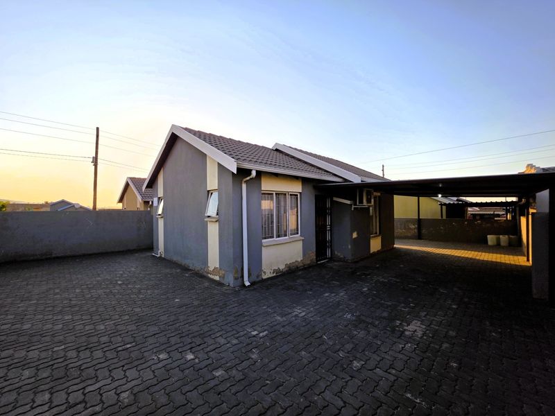 Front exterior view of a detached house featuring a paved driveway, attached carport, and perimeter boundary walling.