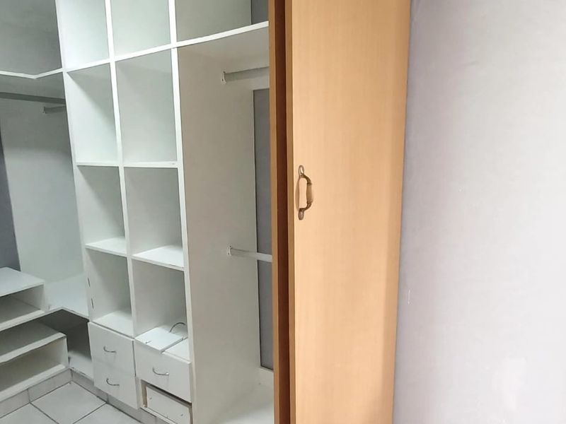 A walk-in closet or dressing area featuring extensive built-in white cabinetry, shelving, and hanging space with tiled flooring.
