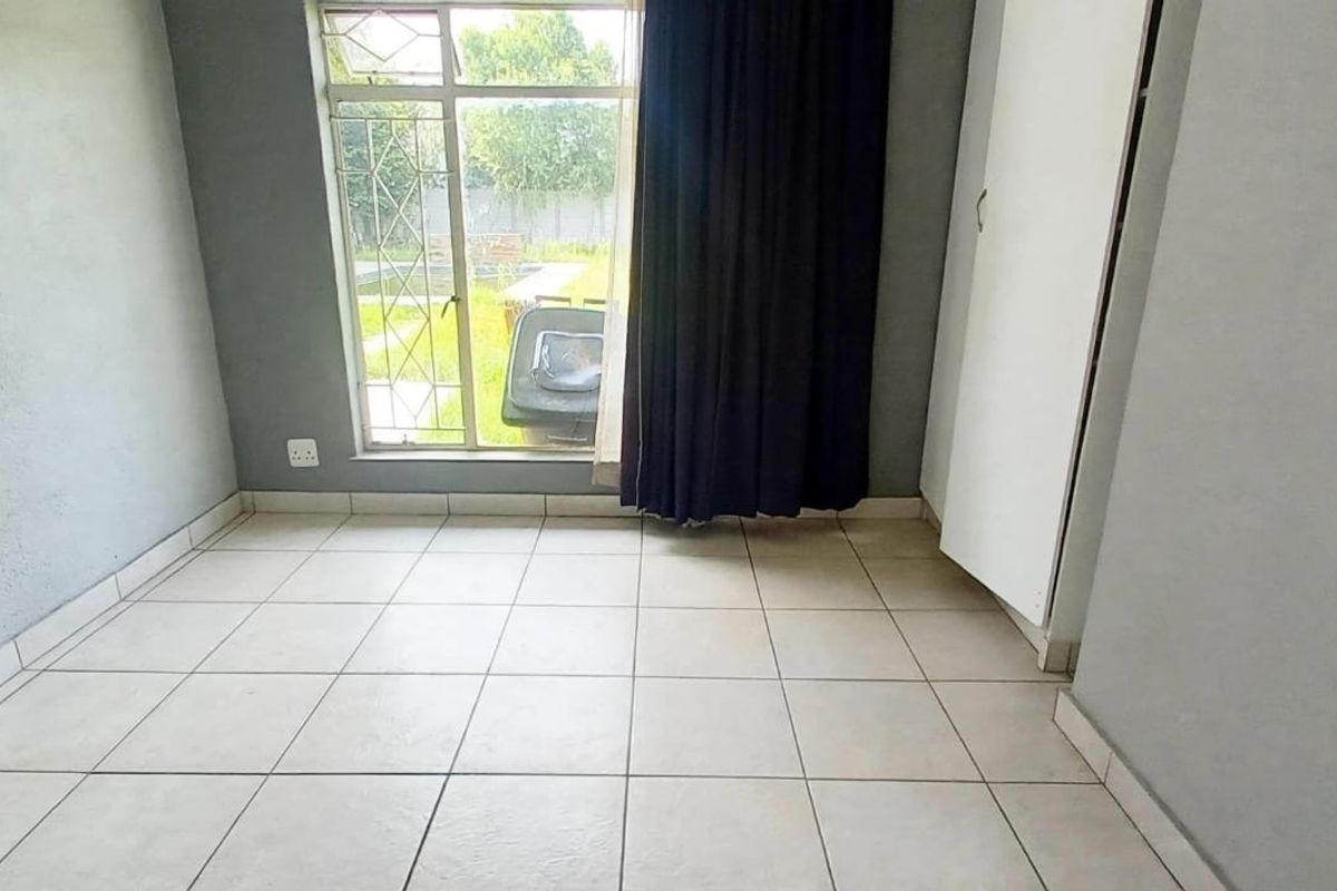 An empty bedroom featuring tiled flooring, a built-in cupboard, and a window with security bars overlooking the rear garden.