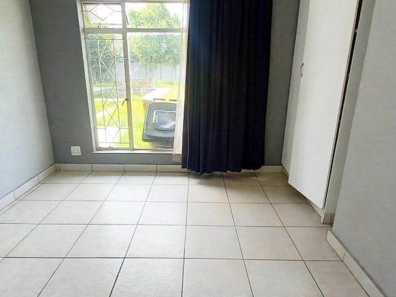 An empty bedroom featuring tiled flooring, a built-in cupboard, and a window with security bars overlooking the rear garden.