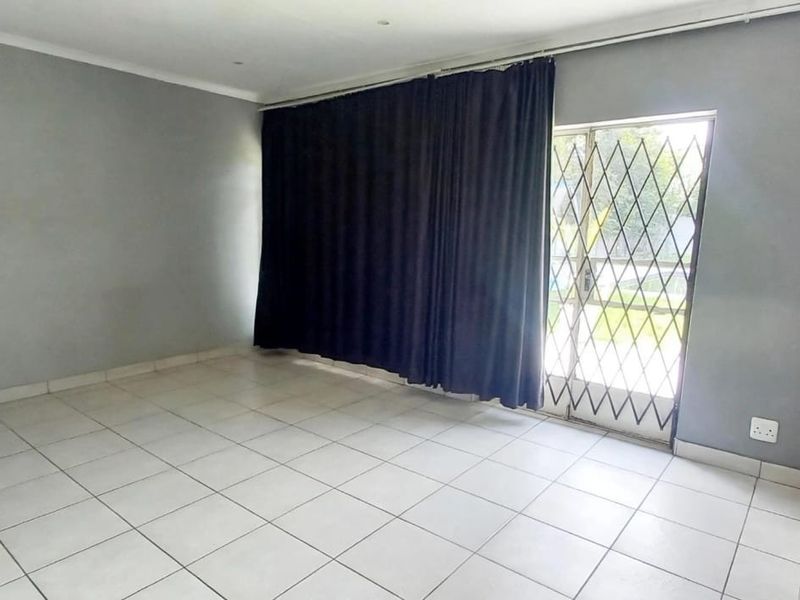 An empty, neutrally painted living room featuring tiled flooring, recessed lighting, and a sliding door with a security gate leading to the exterior.