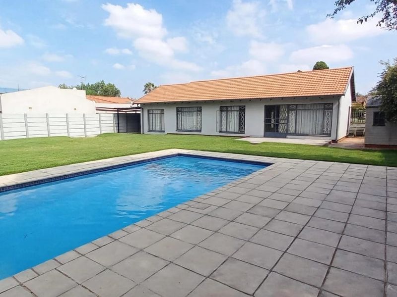 Rear view of the property featuring a swimming pool, paved patio area, and a well-maintained lawn enclosed by precast concrete boundary walls.