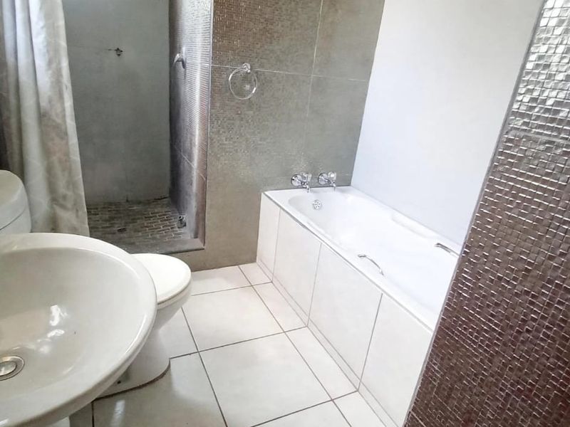 A functional bathroom featuring a built-in bathtub, separate walk-in shower, pedestal basin, and toilet with mosaic wall accents and tiled flooring.
