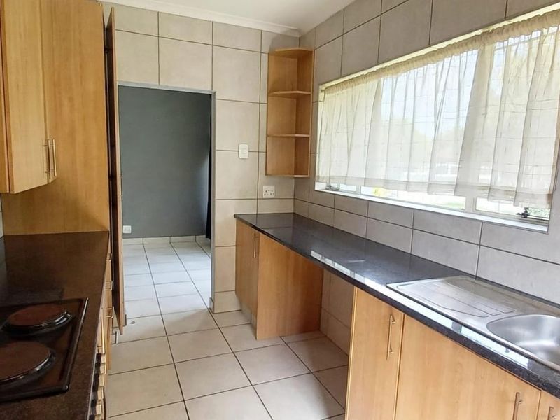 A functional kitchen featuring light wood cabinetry, dark granite countertops, an integrated electric hob, and a stainless steel sink with tiled finishes.