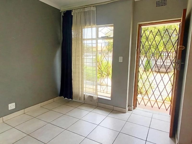 An empty living room featuring tiled flooring, a security gate, and a window with burglar bars, providing direct access to the exterior.