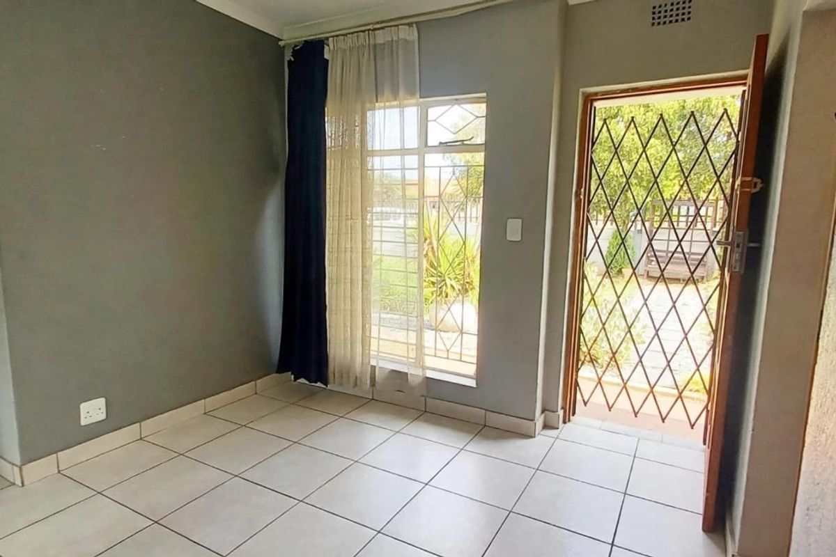 An empty living room featuring tiled flooring, a security gate, and a window with burglar bars, providing direct access to the exterior.