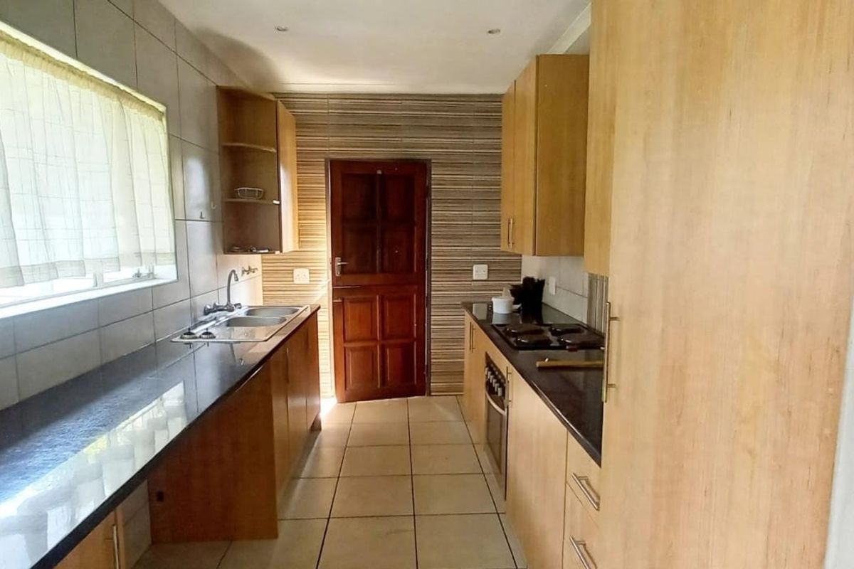A functional galley-style kitchen featuring wooden cabinetry, dark granite countertops, built-in oven and hob, and tiled finishes throughout.