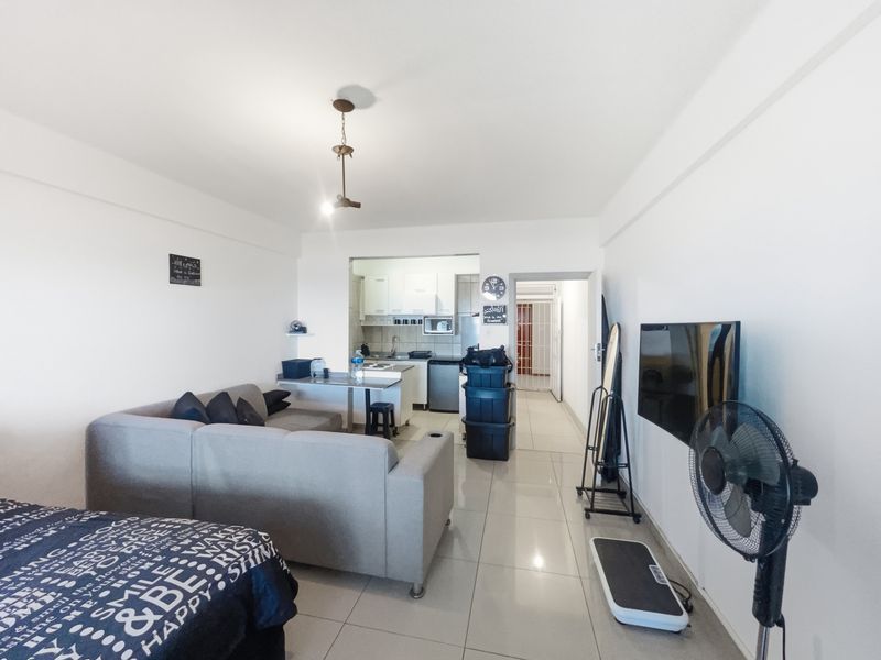 Open-plan living area featuring tiled flooring and a compact kitchen with built-in cabinetry and integrated appliances.