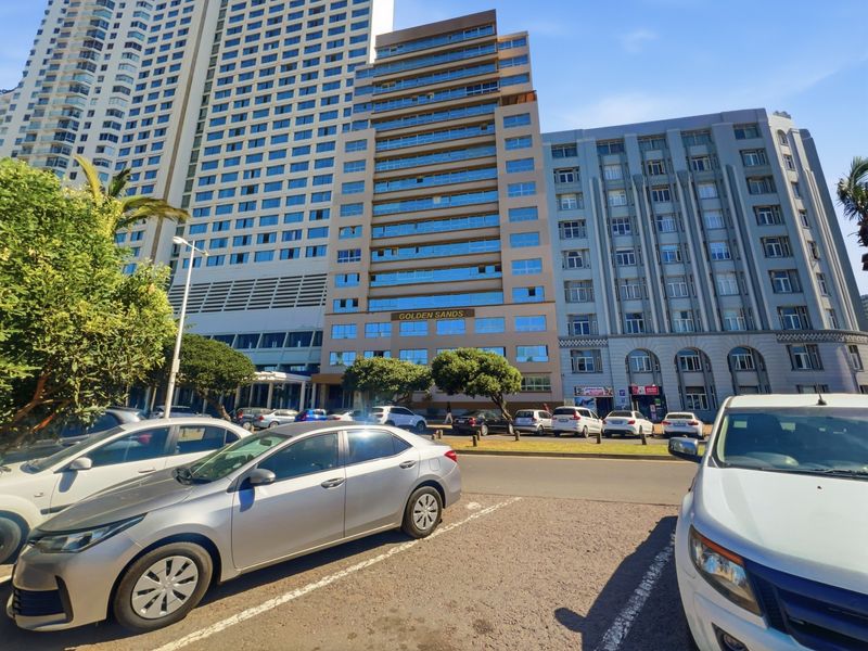 Front exterior view of the Golden Sands multi-story residential building featuring glass balconies and a paved parking area.