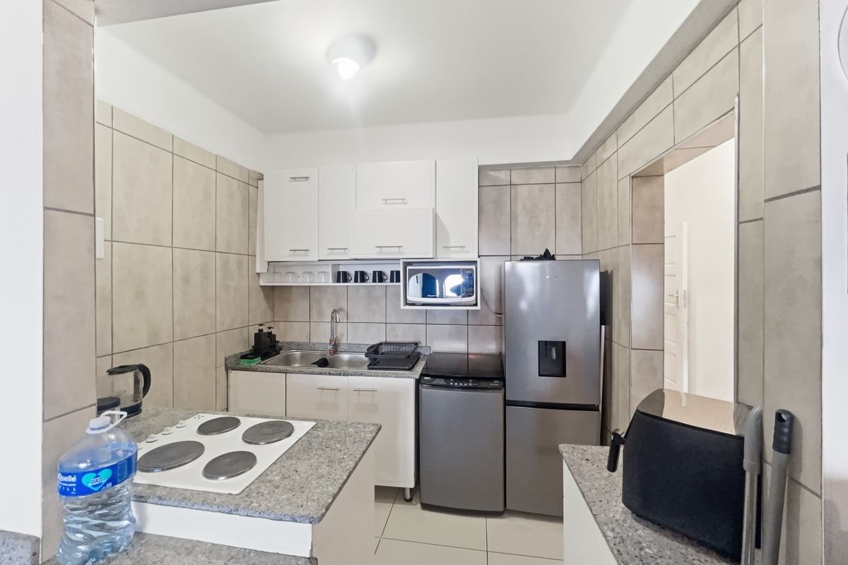Compact kitchen featuring white cabinetry, granite countertops, tiled walls, and an integrated electric hob, providing a functional and efficient cooking space.