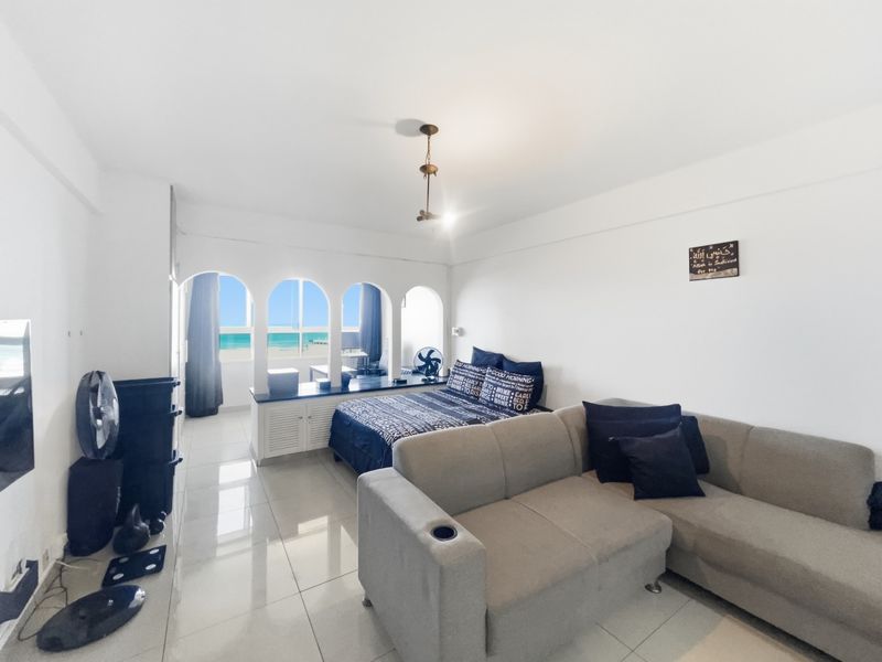 Open-plan living and sleeping area featuring tiled floors, arched window openings with ocean views, and built-in cabinetry.