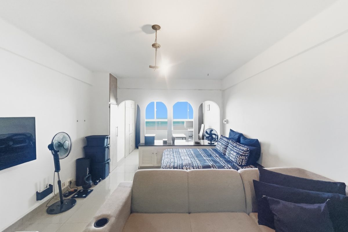 Spacious bedroom featuring built-in cupboards, tiled flooring, and arched windows offering a view of the ocean.