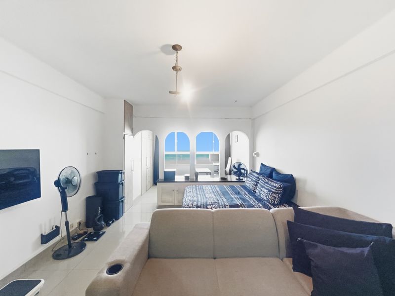 Spacious bedroom featuring built-in cupboards, tiled flooring, and arched windows offering a view of the ocean.
