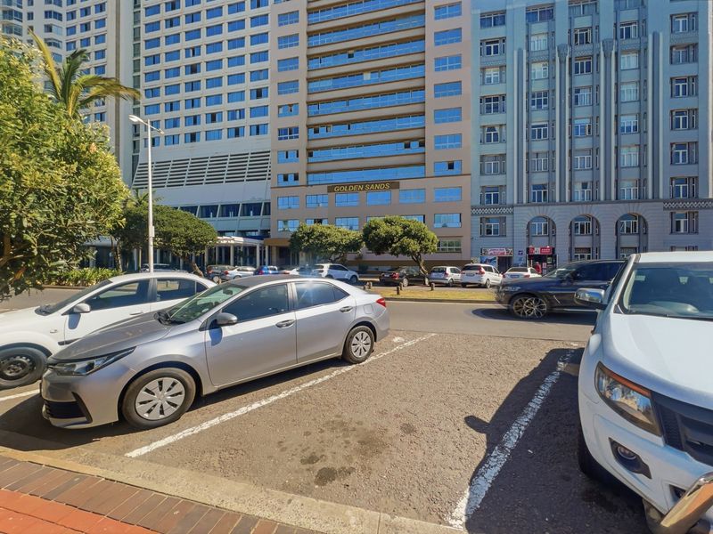 Street-level view of the Golden Sands building facade with adjacent parking area and sidewalk.
