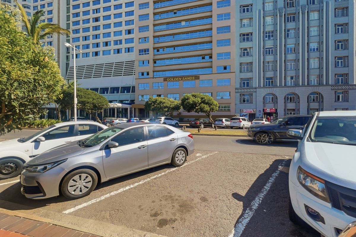 Street-level view of the Golden Sands building facade with adjacent parking area and sidewalk.