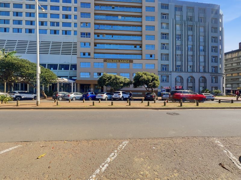Street view of the Golden Sands building facade, featuring a multi-story residential or commercial structure with parking area and road frontage.