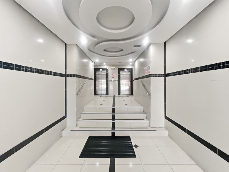 A modern, well-maintained elevator lobby featuring tiled flooring, decorative recessed ceiling details, and stainless steel elevator doors.