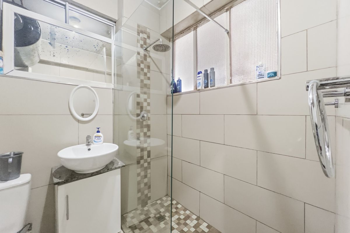 Compact bathroom featuring a glass-enclosed shower, vessel sink with vanity cabinet, and tiled finishes. Requires maintenance on the ceiling and mirror.