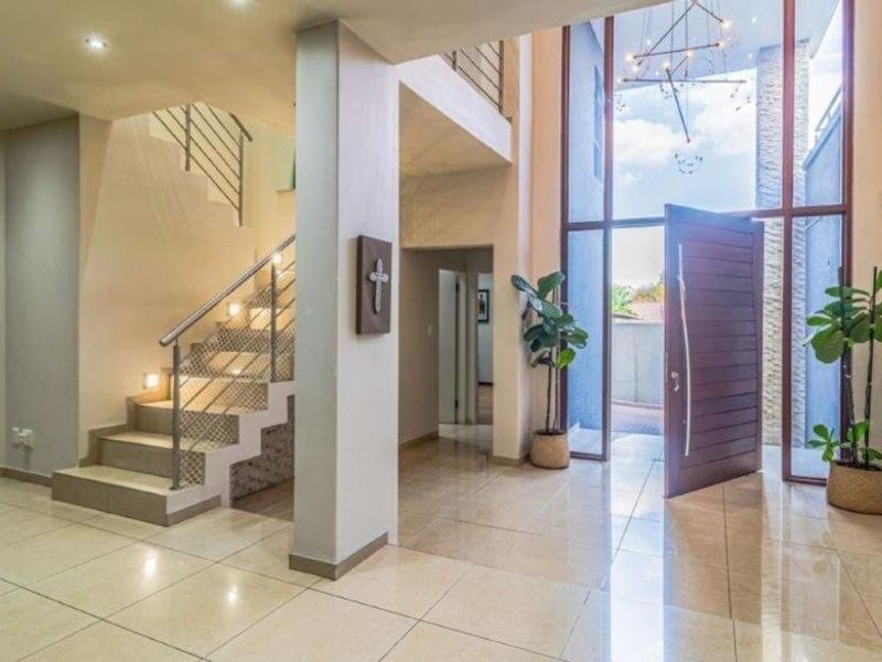 Spacious double-volume entrance hall featuring polished tiled flooring, a modern staircase with stainless steel balustrades, and a grand pivot front door.