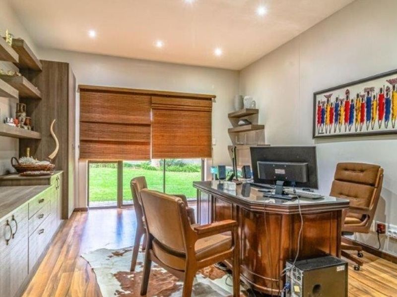 A well-appointed home office featuring custom built-in cabinetry, shelving, laminate flooring, and direct access to the garden through a sliding glass door.