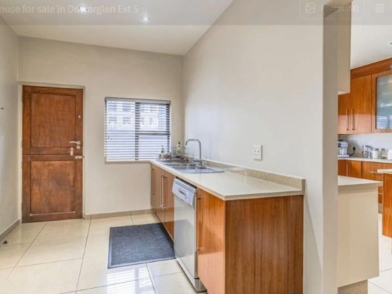 A functional scullery area featuring built-in wooden cabinetry, laminate countertops, a stainless steel sink, and tiled flooring, adjacent to the main kitchen.