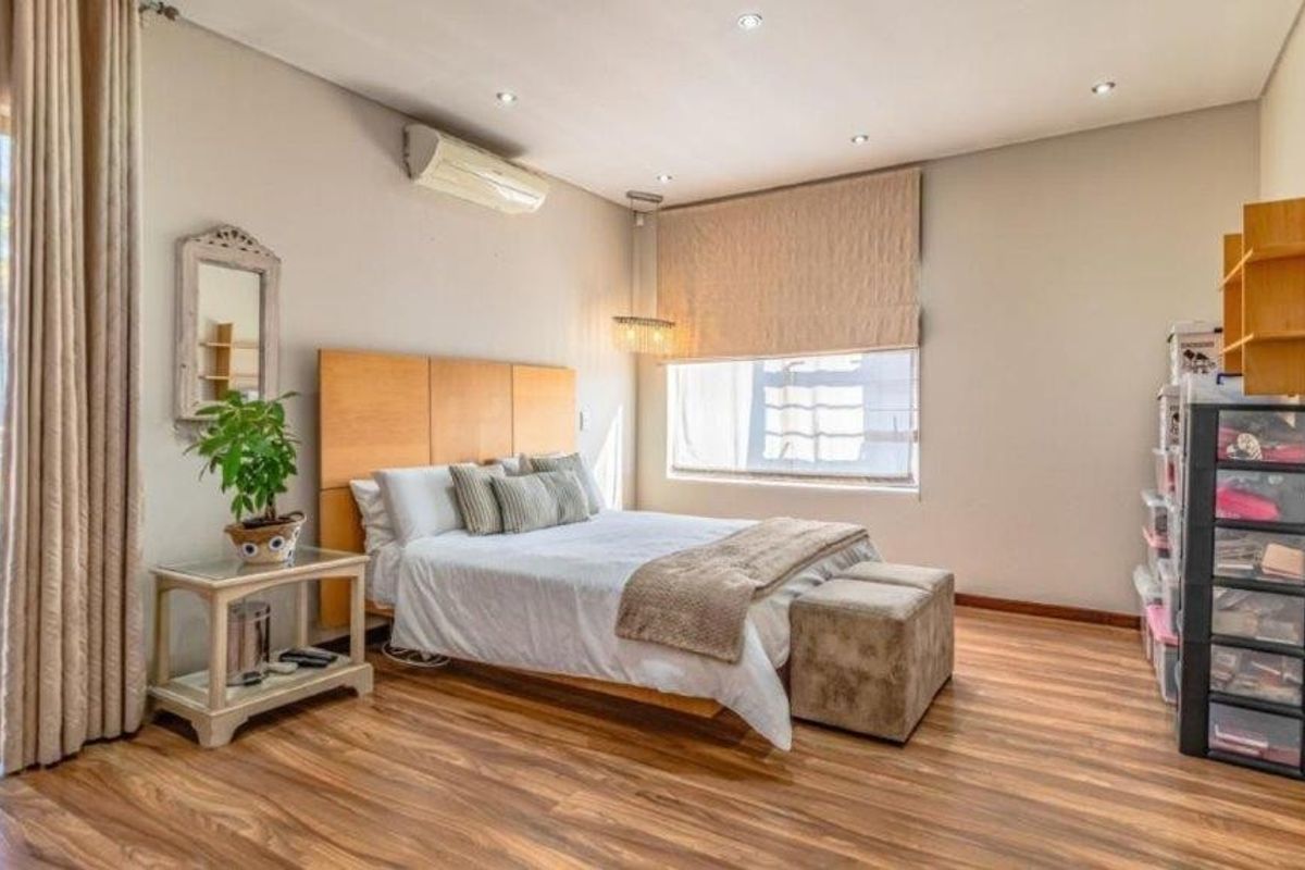 A well-maintained bedroom featuring laminate flooring, recessed lighting, a wall-mounted air conditioning unit, and direct access to an outdoor area via sliding glass doors.