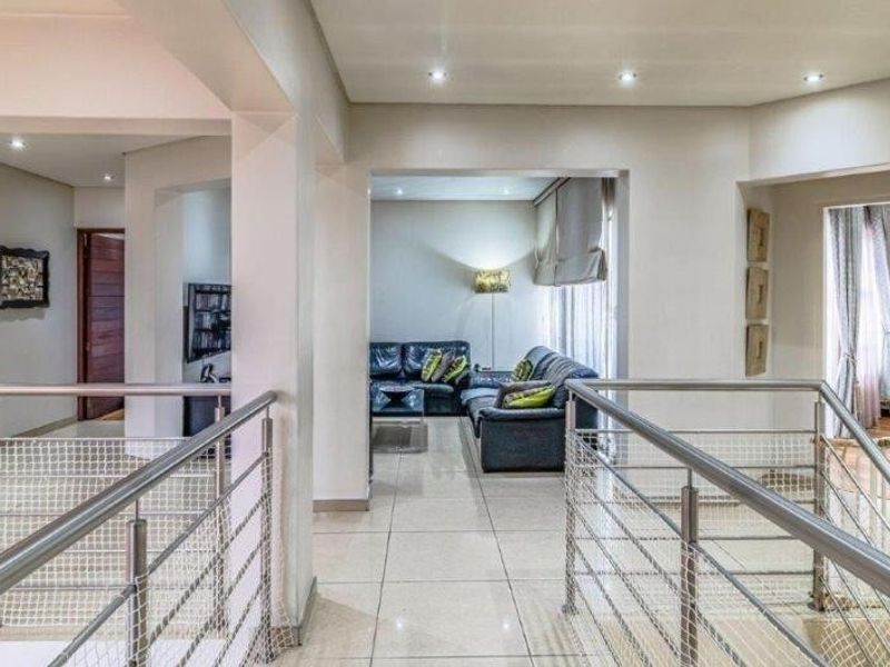 A spacious upper-level landing area featuring modern stainless steel balustrades, tiled flooring, and recessed lighting, providing access to adjacent living spaces.