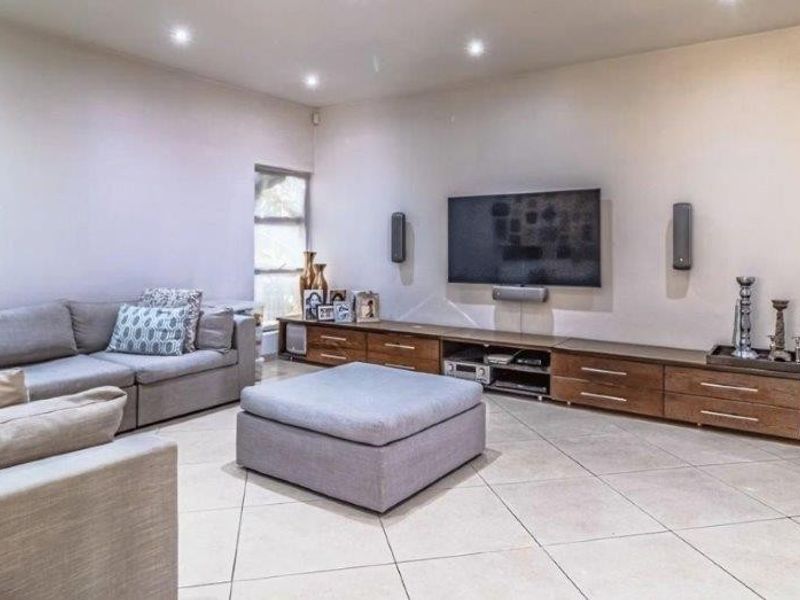 A spacious living room featuring neutral tiled flooring, recessed downlighting, and extensive built-in media cabinetry along the main wall.