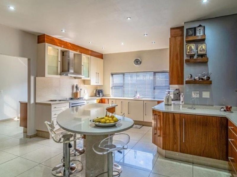 Modern kitchen featuring wood-toned cabinetry, stone countertops, a central island, built-in oven, and recessed lighting, offering a functional and well-maintained cooking space.