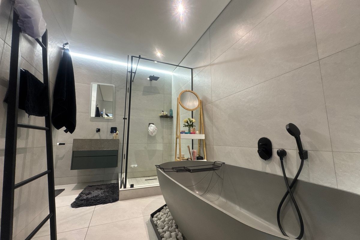 Modern, high-end bathroom featuring a sleek freestanding bathtub, a spacious walk-in shower with black fixtures, and contemporary wall-mounted vanity with ambient LED lighting.