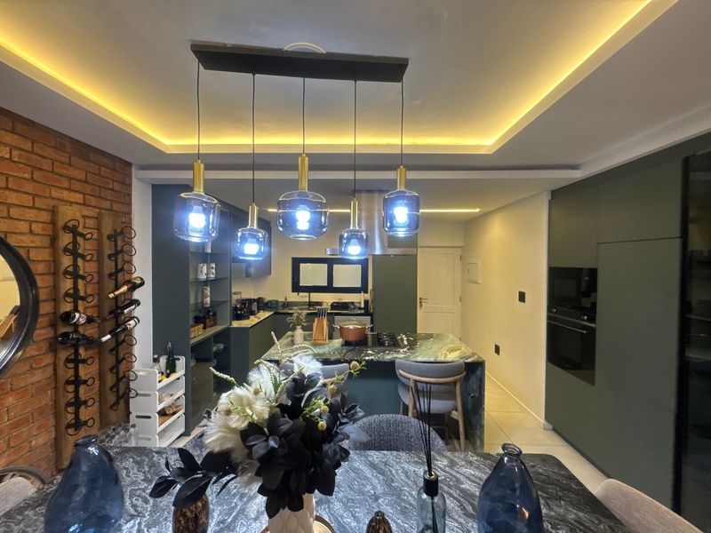 Modern open-plan kitchen featuring a stone-topped island, integrated appliances, sleek cabinetry, and stylish pendant lighting with an exposed brick feature wall.