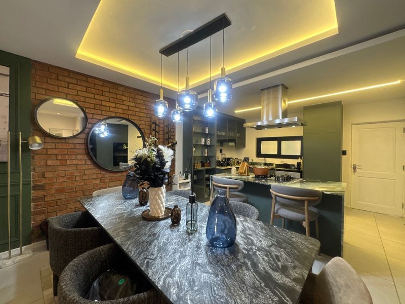 Modern open-plan living and dining area featuring an exposed brick wall, stylish pendant lighting, and a contemporary kitchen with a stone-topped island.