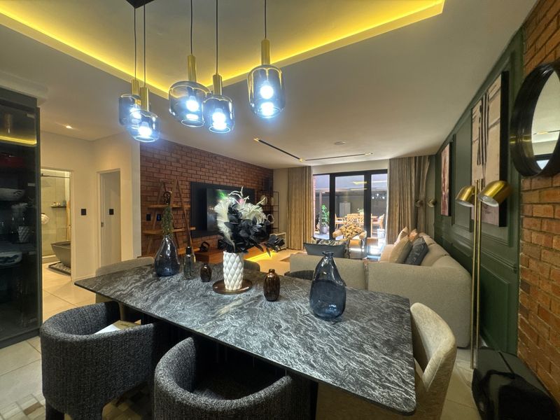 Modern open-plan living and dining area featuring an exposed brick wall, sophisticated recessed lighting, and seamless access to the outdoor patio space.