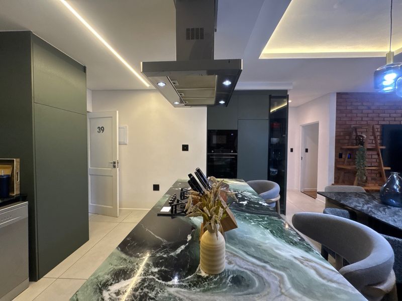 Modern open-plan kitchen featuring a striking stone-topped island, integrated appliances, recessed lighting, and a stylish exposed brick accent wall.
